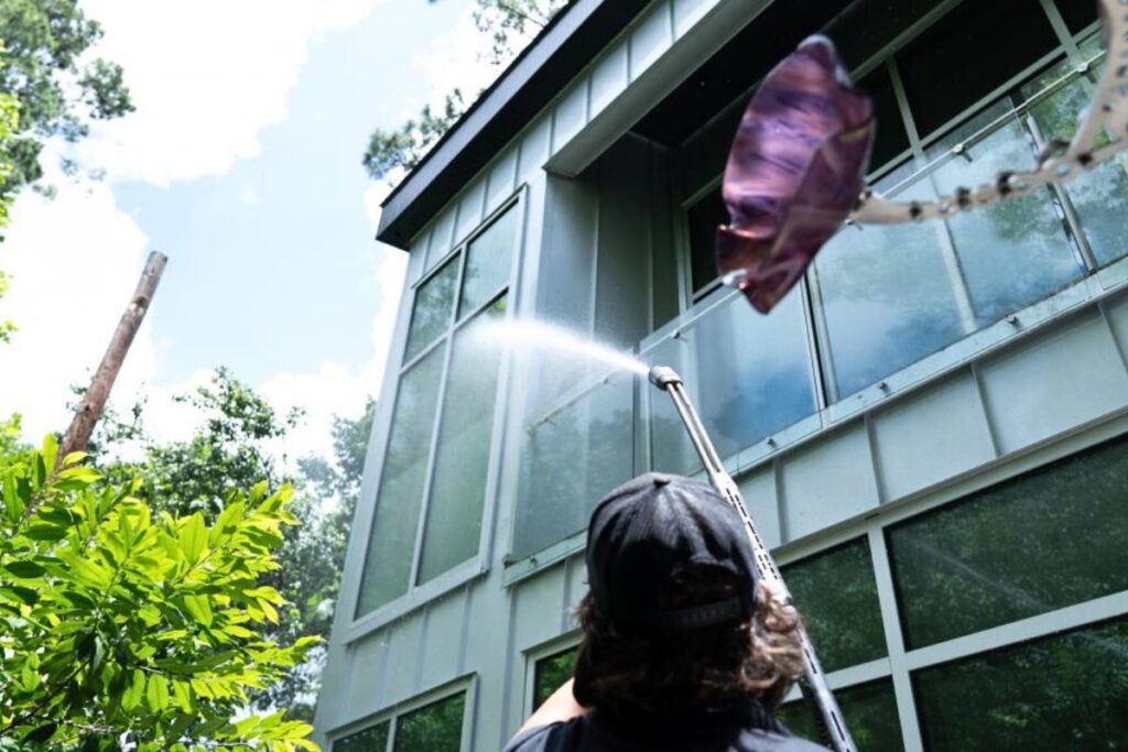 man cleaning glass window using power washing